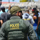 A Border Patrol agent walks along a line of migrants waiting to turn themselves in for processing, in El Paso, Texas